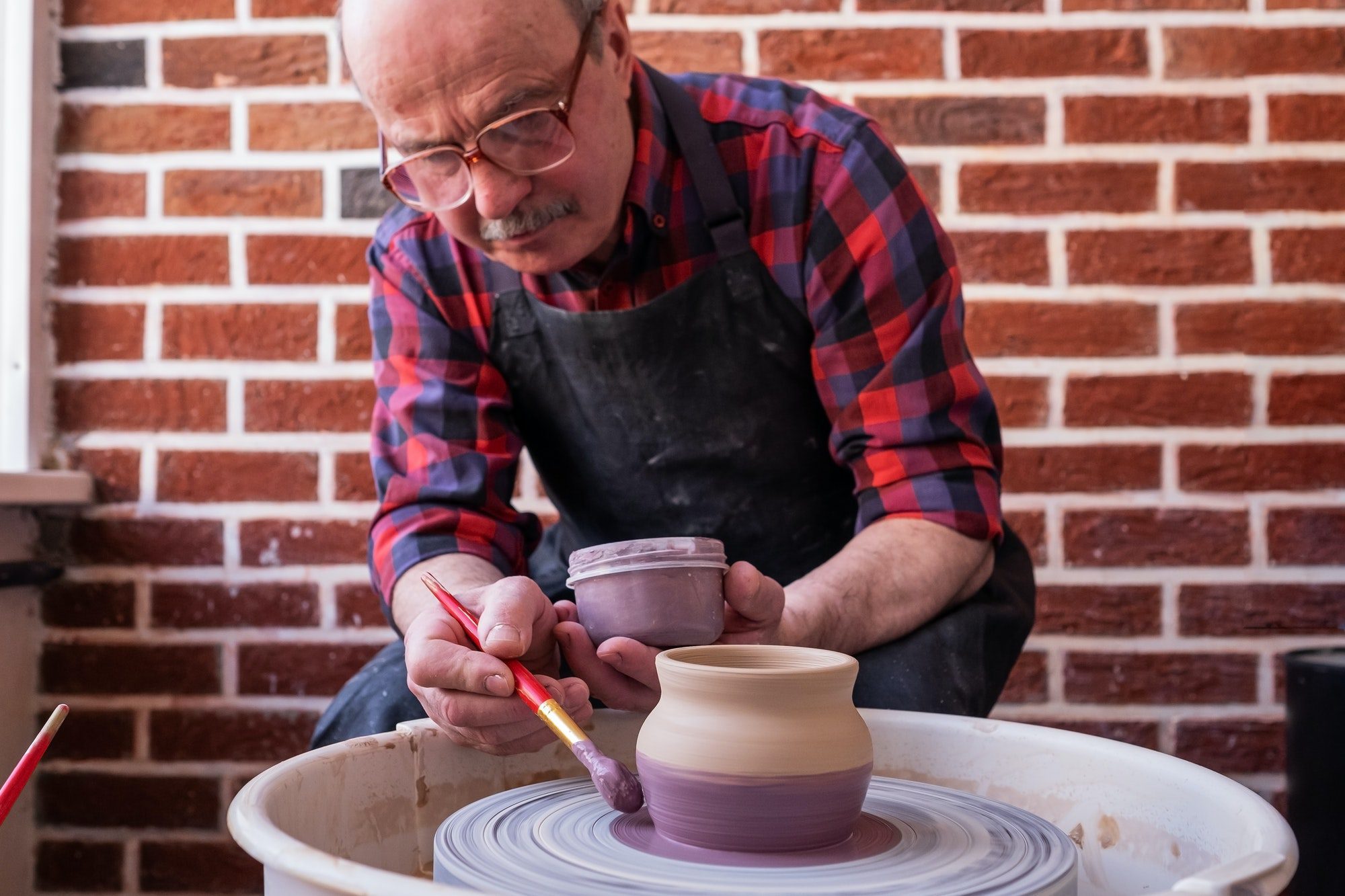 senior man holding a brush painting on a ceramic using potter wheel