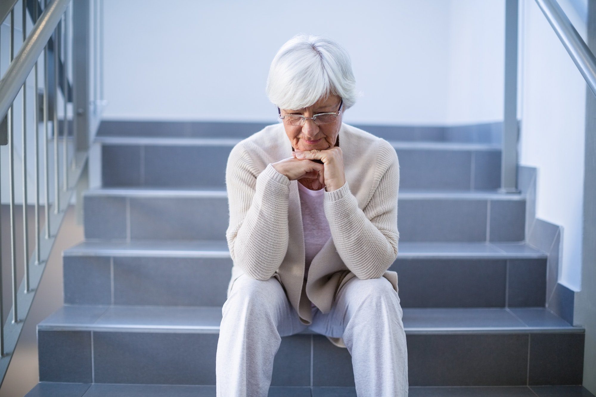 Upset senior woman sitting on stairs pondering how she is going to pay for the 2022 Medicare premium hike.