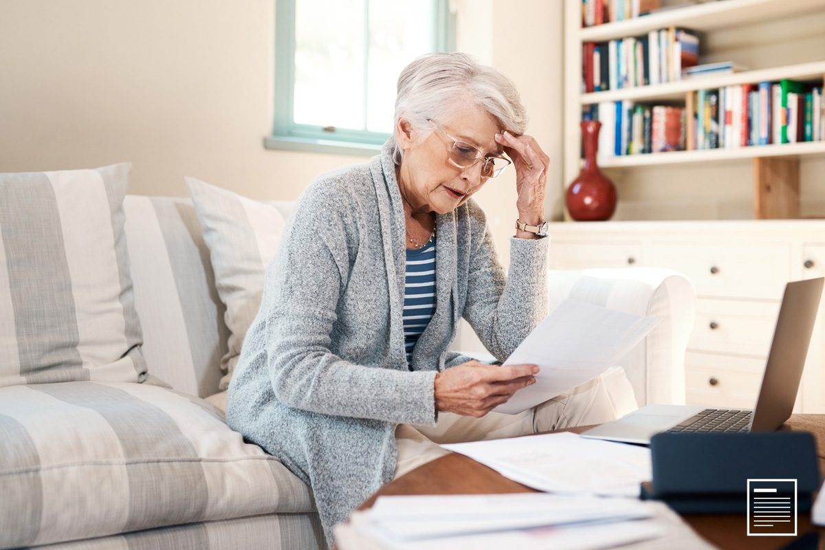 An elder lady sitting on a couch going over her Cancer Patient Eligible Medicare form.