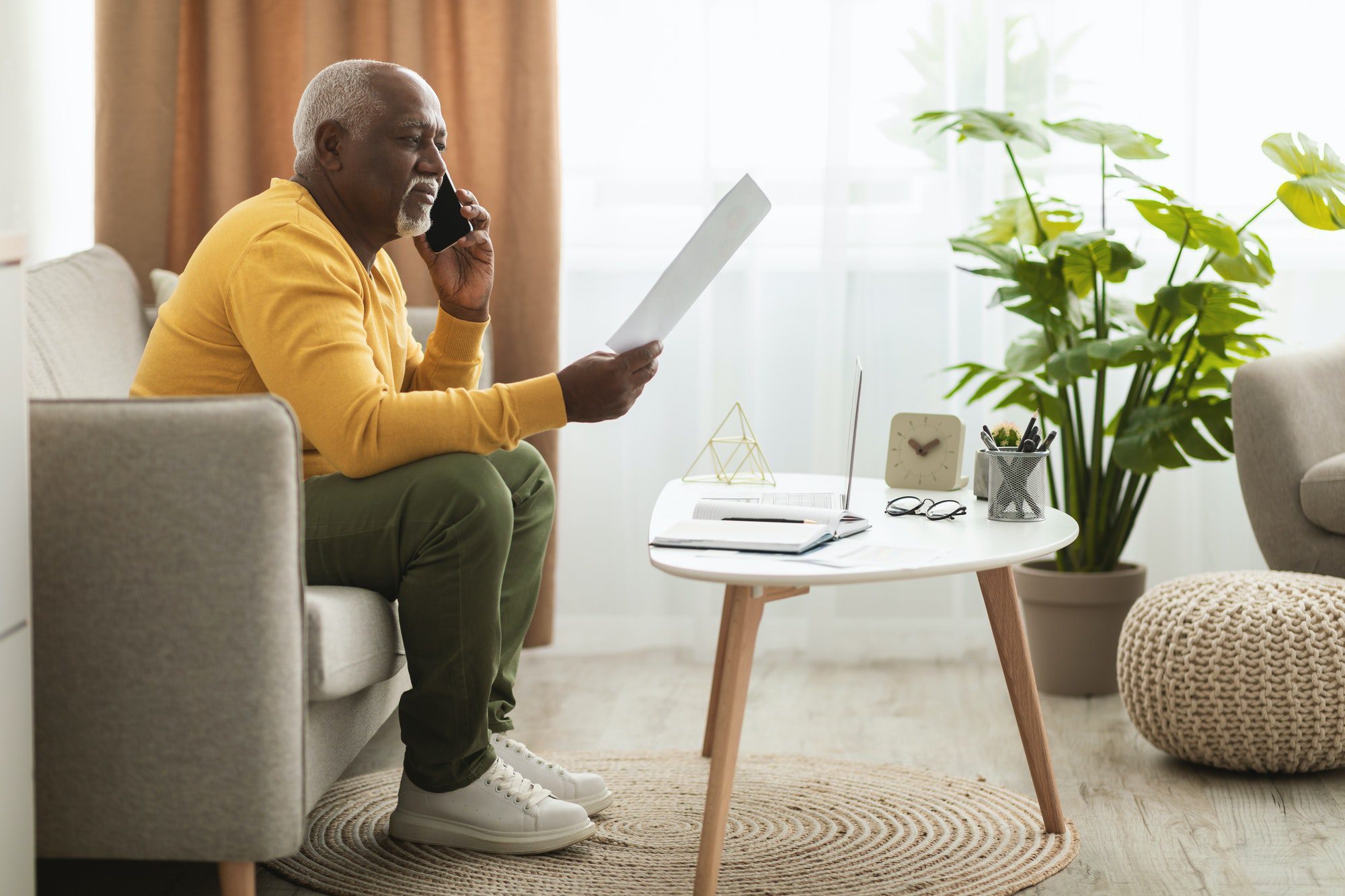 Senior African Businessman Talking On Phone Holding Paper Indoors, Side-View wondering if he has Medicare Eligibility Requirements
