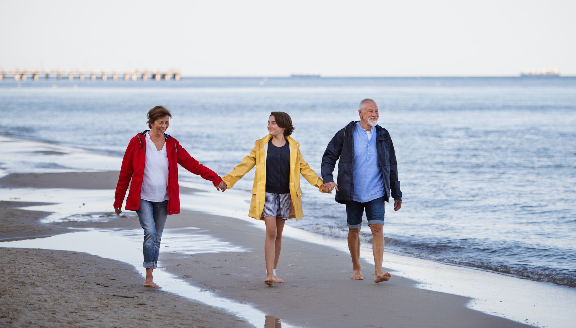 Senior couple holding hands with their preteen granddaughter and walking on sandy beach with Medicare Advantage Plan